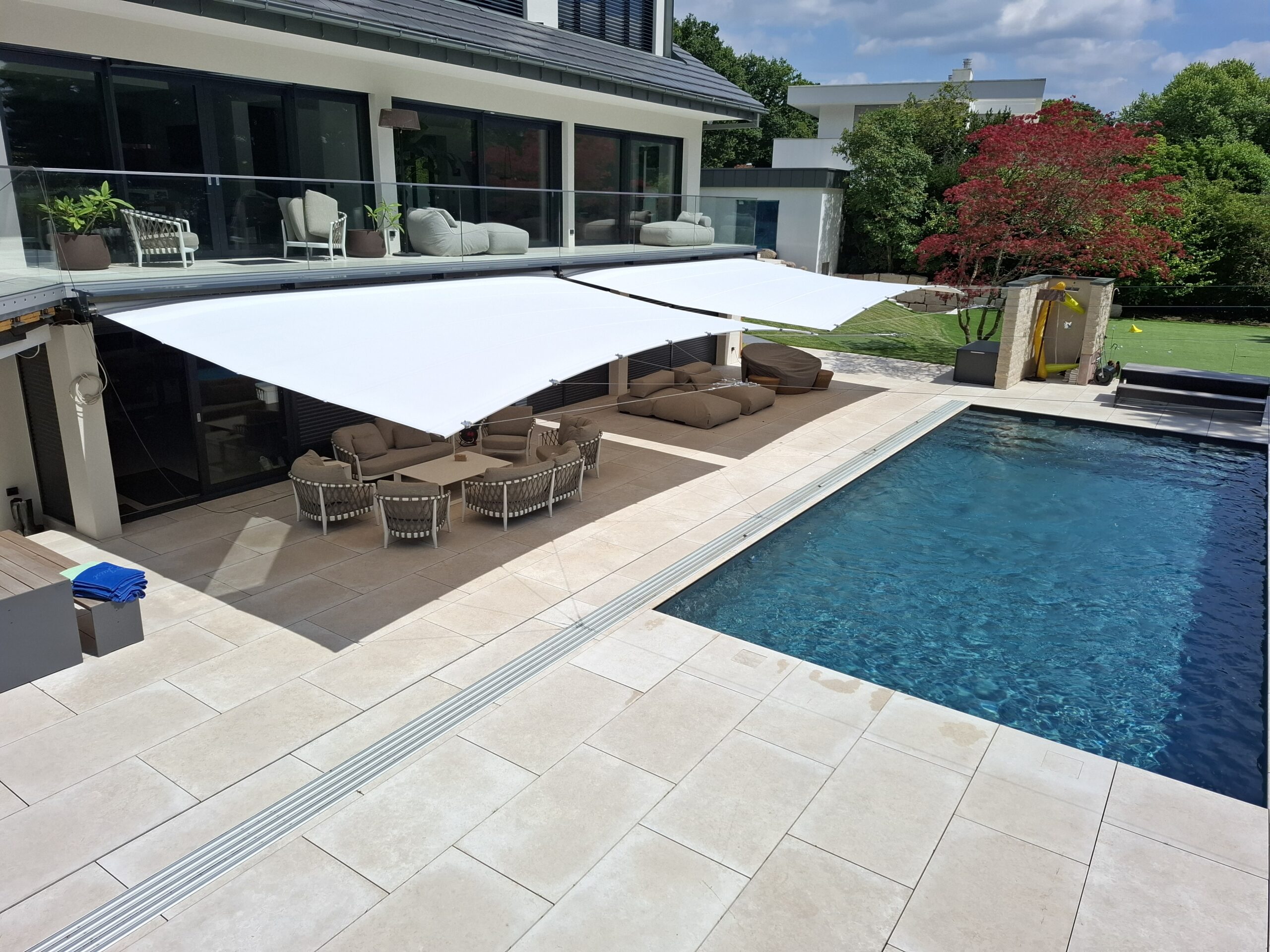 Wide Öhrra Square retractable shade sails extended over outdoor seating beside a swimming pool